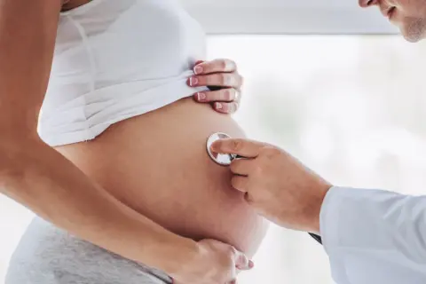 Lekarz osłuchuje brzuch kobiety w 24 tygodniu ciąży. Słychać bicie serca dziecka.