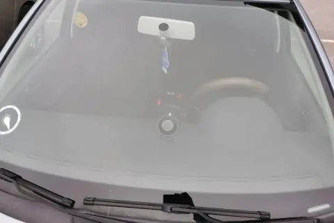 Bilens vindruta med en glad smiley-halsduk, backspegel och en dashcam. Perfekt för en stenskott besiktning.