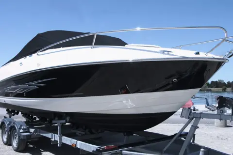 Barca sportiva bianca e nera su carrello, pronta per il varo. I candelieri sono i supporti metallici che la tengono ferma.