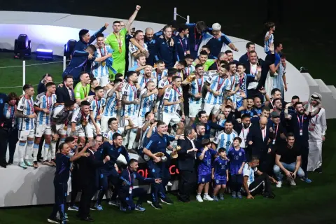 Piłkarze Argentyny świętują zwycięstwo, trzymając puchar. Wszyscy w biało-niebieskich strojach, z medalami na szyjach, tworzą najlepszą drużynę na świecie.