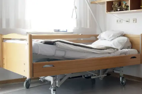 Ein Pflegebett mit Holzrahmen und Rädern, bereit, wenn Sie ein Pflegebett beantragen müssen.