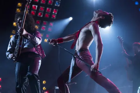 Freddie Mercury śpiewa "Bohemian Rhapsody", a jego zespół gra na żywo. Nuty tej ikonicznej piosenki rozbrzmiewają na koncercie.