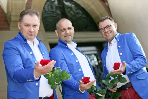 Trzech panów w niebieskich marynarkach, czyli skład zespołu Blue Party, prezentuje czerwone róże.