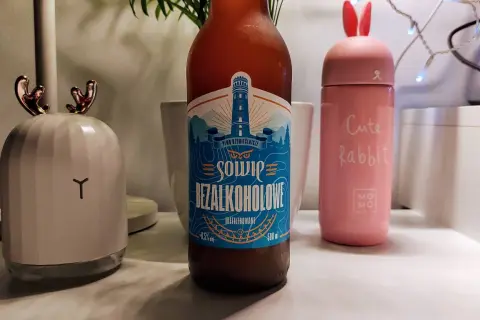 Piwo bezalkoholowe o smaku piwa, z etykietą latarni morskiej. Obok różowy kubek "Cute Rabbit" i lampka w kształcie głowy renifera.