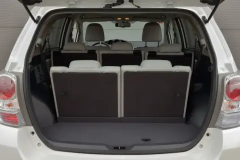 Biała Toyota Verso 1.8 benzyna z otwartym bagażnikiem. Tylne siedzenia złożone, tworząc dużą przestrzeń bagażową.