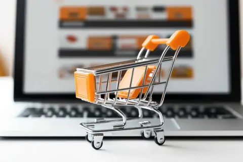 Miniaturowy wózek na zakupy przed ekranem laptopa symbolizuje najpopularniejsze sklepy internetowe i wygodne zakupy online.