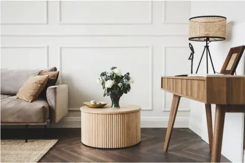 Elegancki salon glamour z dominującym drewnem. Miękka sofa, okrągły stolik i stylowe biurko tworzą przytulną przestrzeń.