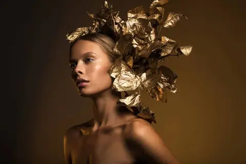 A model with a golden leaf headdress, captured with dramatic fashion lighting photography, showcasing a radiant glow.