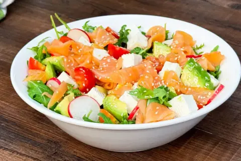 Insalata fresca con salmone affumicato, avocado, pomodorini, ravanelli e cubetti di formaggio, cosparsa di semi di sesamo.