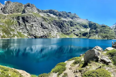 Le lac de Caillauas, d'un bleu profond, reflète les montagnes escarpées et verdoyantes sous un ciel clair. Une structure rocheuse rappelle un château sur la rive.