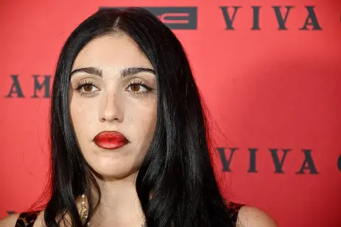 Lourdes Leon, con labbra rosse audaci e sguardo intenso, posa davanti a uno sfondo rosso con scritte nere.