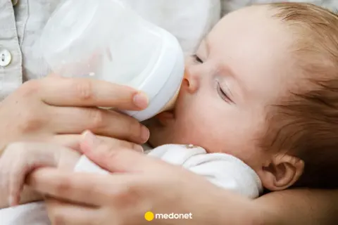 Dziecko pije mleko modyfikowane z butelki. Mama karmi maluszka, który spokojnie zasypia.