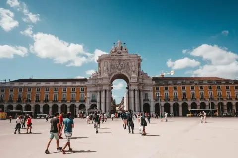En solig dag på ett stort torg i Lissabon, Portugal. Människor promenerar under en imponerande triumfbåge. Ett perfekt restips för Portugal.