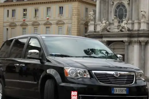 Czarny Lancia Voyager na tle zabytkowej architektury.