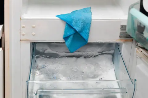 W zamrażarce lodówki no frost nagromadził się lód, a niebieska ściereczka czeka na rozmrożenie.