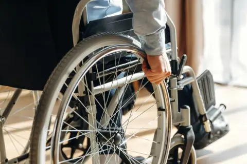 Dłoń osoby niepełnosprawnej chwyta obręcz wózka inwalidzkiego, gotowa do samodzielnego ruchu.