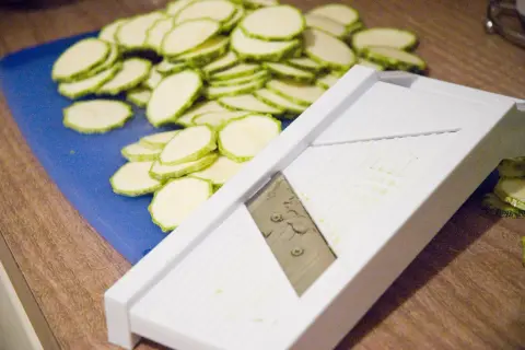 En hög med skivade squash ligger bredvid en bra mandolin.