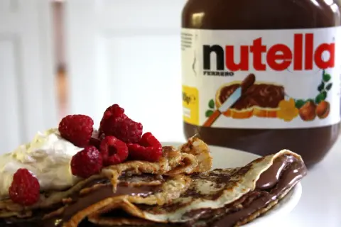 En pannkakstårta med nutella, grädde och hallon. En burk nutella syns i bakgrunden.
