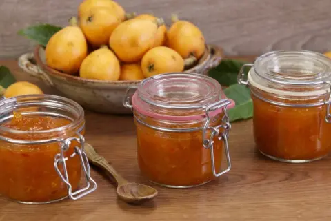 Tre barattoli di marmellata di nespole fatti in casa, con nespole fresche in una ciotola sullo sfondo.