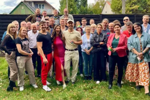 Uśmiechnięta obsada serialu "Barwy szczęścia" 2025 pozuje do wspólnego zdjęcia na trawie.