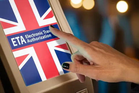 Dłoń dotyka ekranu z flagą Wielkiej Brytanii i napisem ETA. Elektroniczna autoryzacja podróży do Wielkiej Brytanii.