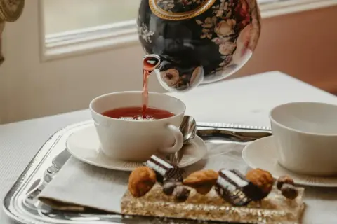 Tetera floral vierte té rojo en taza blanca. Bandeja con dulces y otra taza, perfecto para la hora del té en Inglaterra.