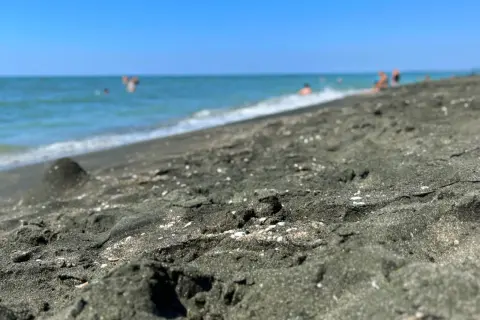 Ciemny piasek na plaży w Ureki, Gruzja. W tle widać turkusowe morze i kąpiących się ludzi.