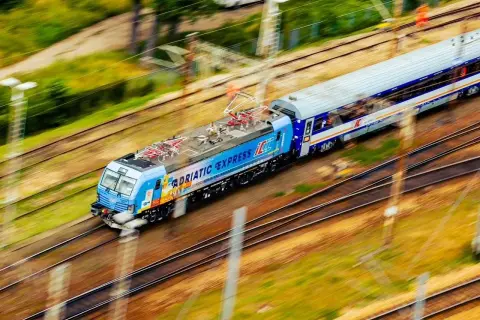 Pędzący pociąg "Adriatic Express" na trasie z Warszawy do Łodzi, z rozmytym tłem zieleni i torów.
