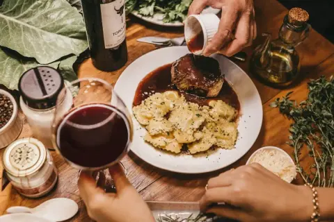 Elegancka kolacja: steka w sosie winnym, ravioli, kieliszek czerwonego wina. Idealny moment, kiedy dodać wino do mięsa, by wzbogacić smak.