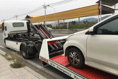 Pomoc drogowa w akcji: białe auto jest ładowane na lawetę. Widać, jak holować auto, gdy jest potrzebna pomoc.