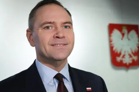 Polityk w garniturze z polskim godłem w tle.