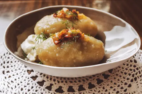 Cepelinai, comida típica de Lituania, servidos con crema agria y tocino crujiente.