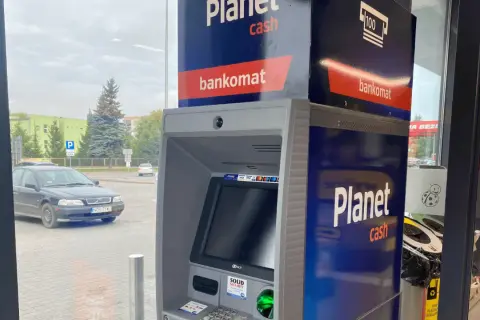 Bankomat Santander Planet Cash przy parkingu. Obok stoi czarny samochód.