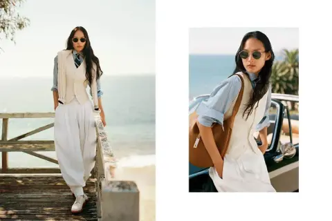 Donna in stile smart casual con pantaloni bianchi ampi, gilet e camicia azzurra, con un tocco di eleganza sulla passerella vista mare.