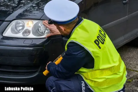 Policjant sprawdza światła samochodu, w tym światła przeciwmgielne. W ręku trzyma miernik.
