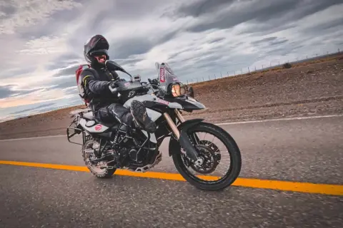 Motocyklista w kasku i kurtce pędzi na motocyklu BMW F 800 po pustej drodze pod burzowym niebem.