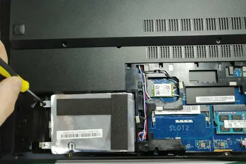 Ręka przykręca śrubkę mocującą dysk SSD w laptopie. Poradnik: jak zamontować dysk SSD.