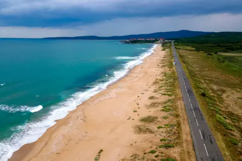 Bułgaria jakie morze? Piękna, turkusowa woda obmywa piaszczystą plażę, a w oddali widać zabudowania i zielone wzgórza. Droga wzdłuż wybrzeża zaprasza do podróży.