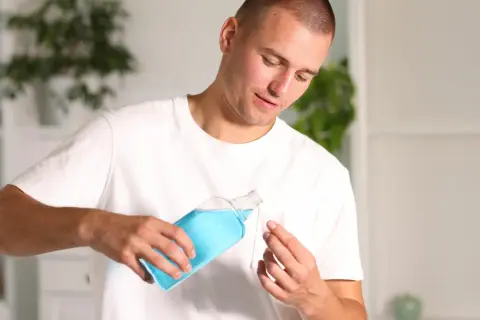Uomo versa collutorio con clorexidina in un bicchierino.