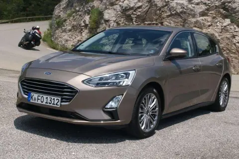 Brązowy Ford Focus 2017 na krętej drodze, z motocyklistą w tle.