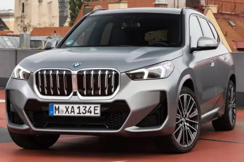 Srebrny x1 bmw z charakterystyczną atrapą chłodnicy i nowoczesnymi światłami, zaparkowany na tle miejskiej panoramy.