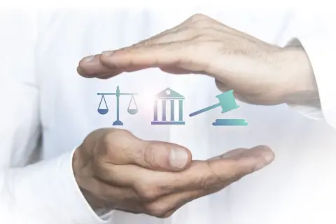 Mains protégeant des icônes symbolisant la justice : balance, bâtiment de tribunal, marteau de juge. L'image évoque l'importance de l'état de droit.