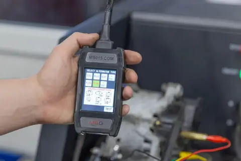 Dłoń trzyma tester diagnostyczny do alternator w samochodzie. Ekran pokazuje wybór typu alternatora i połączeń LIN/BSS.