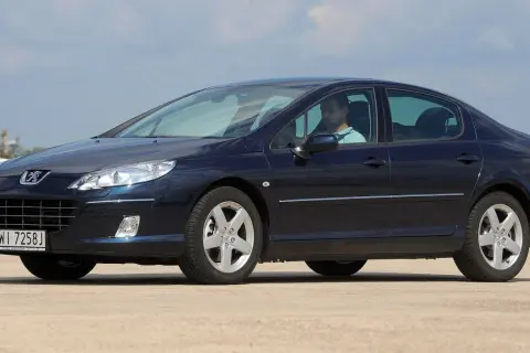 Ciemnoniebieski Peugeot 407 z widocznymi żarówkami reflektorów, kierowca za kierownicą.