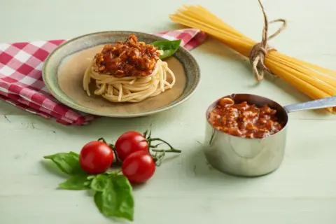 Pyszny sos do spaghetti przepis na talerzu, obok pomidorki i makaron.