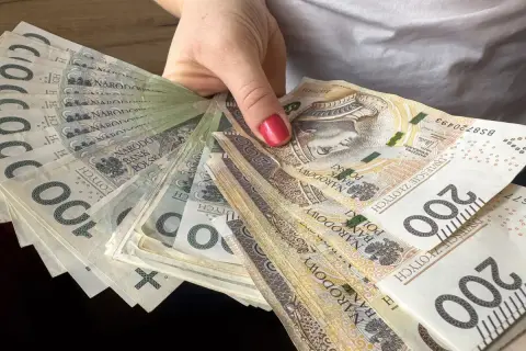 Dłoń trzyma wachlarz polskich banknotów 100 i 200 zł. To może być nagroda jubileuszowa nauczycieli.