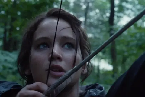 Katniss Everdeen spänner sin båge i skogen, redo för kampen i hunger games filmserie.
