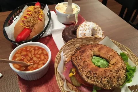 Un bagel de l'ouest garni de viande, salade et cornichons, accompagné d'un hot-dog, de haricots à la tomate, de salade de chou et de deux donuts.