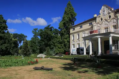 Pałac w Witaszycach, dawniej hotel, otoczony zielenią. Na trawniku leży zabytkowa armata.
