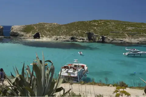 Malta co warto zobaczyć: Błękitna Laguna na Comino, z krystalicznie czystą wodą, łodziami i skalistymi klifami. Idealne miejsce na relaks.